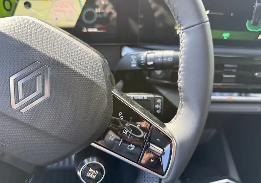 Gros plan sur le volant cuir gris de la Renault Clio VI TCe 115 Techno, avec commandes intégrées et bouton Multi Sense visible.