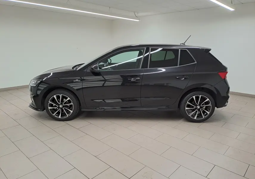 Profil côté gauche d'une Skoda Fabia 2024 noire Magic Nacré avec jantes alliage et finition Monte-Carlo dans un intérieur lumineux.