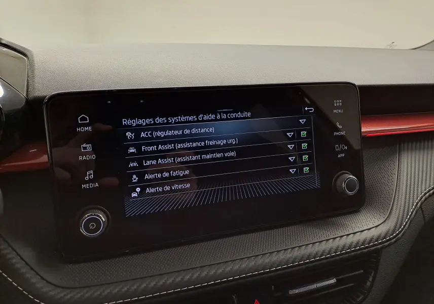 Écran tactile central de la Skoda Fabia 2024 affichant les réglages des aides à la conduite, intérieur noir avec bande rouge.