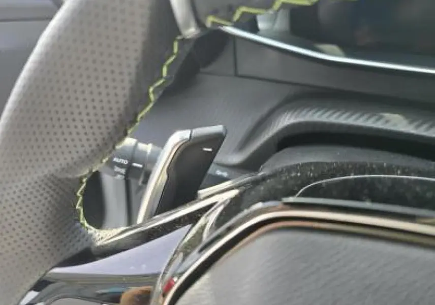Gros plan sur le volant cuir perforé avec surpiqûres vertes et palettes de changement de vitesse du Peugeot 2008 hybride 2025.