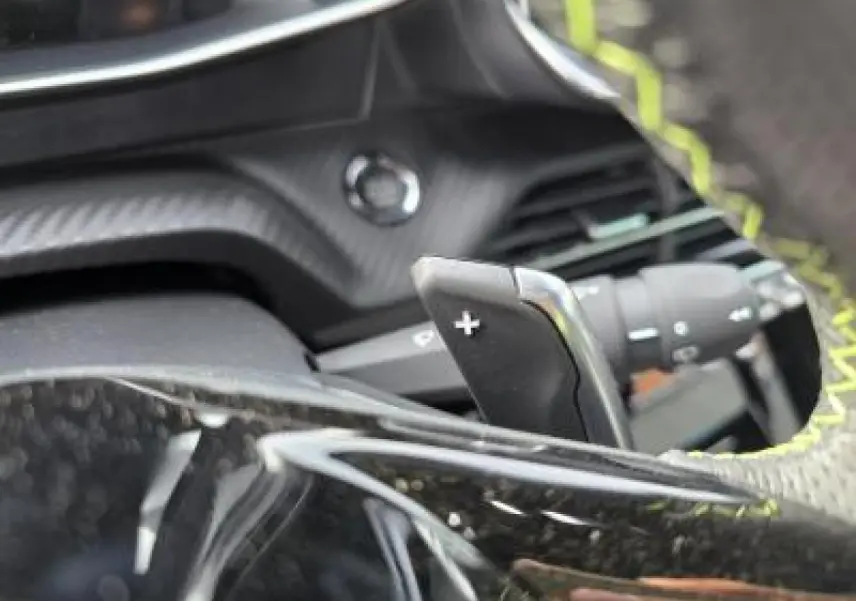 Gros plan sur la palette de changement de vitesse + du volant au cuir noir avec surpiqûres vertes du Peugeot 2008 hybride blanc.