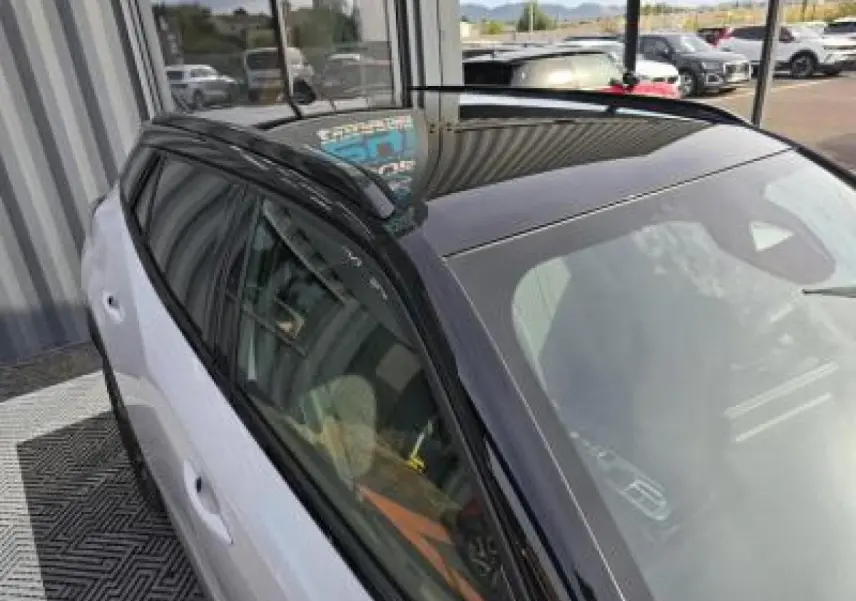 Peugeot 2008 hybride 2025 blanc Okenite toit noir en vue 3/4 arrière côté gauche avec barres de toit noires.