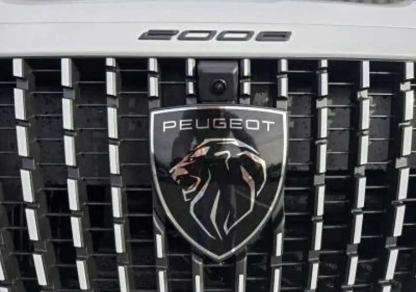 Gros plan sur la calandre noire brillante du Peugeot 2008 blanc Okenite avec logo lion et inscription 2008 au-dessus.