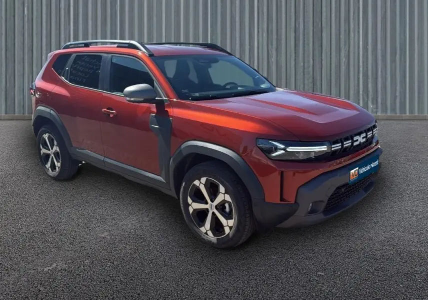Vue 3/4 avant droit d'un Dacia Duster orange 2025 avec barres de toit et jantes alliage 18 pouces.