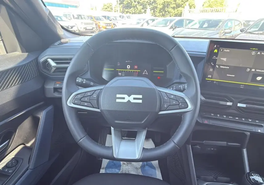 Vue intérieure centrée sur le volant multifonction et le tableau de bord numérique du Dacia Duster 2025.