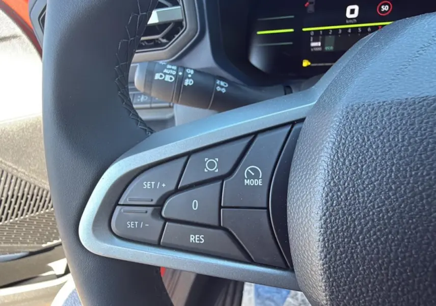 Gros plan sur les commandes du régulateur de vitesse au volant du Dacia Duster orange 2025 côté gauche.