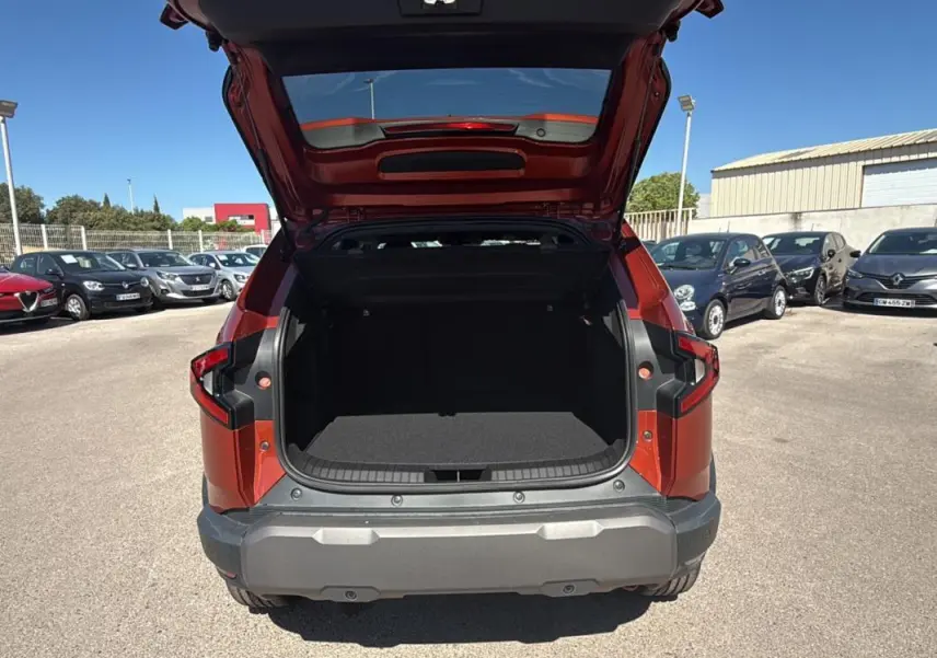 Vue arrière d'un Dacia Duster orange 2025 avec coffre ouvert, soulignant l'espace de chargement et les feux arrière distinctifs.