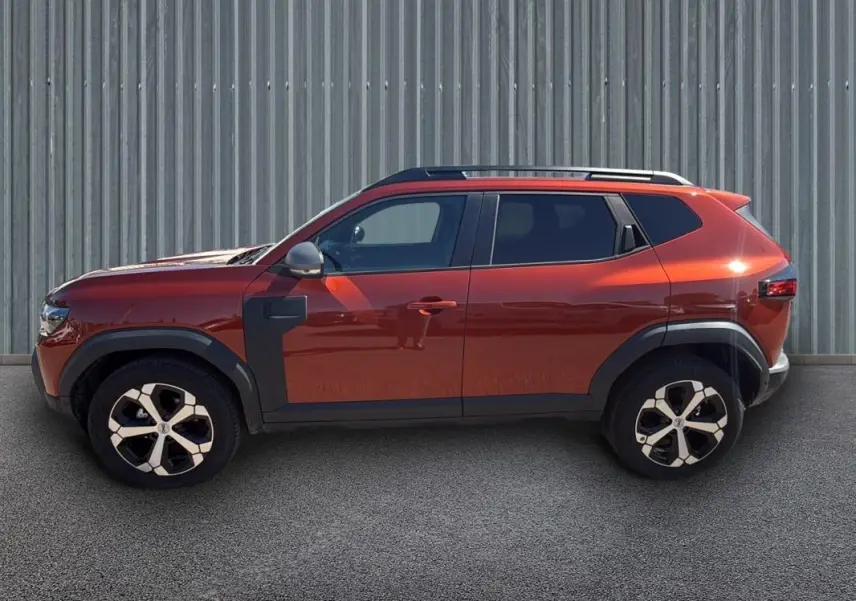 Profil côté gauche du Dacia Duster 2025 orange avec barres de toit et jantes alliage 18 pouces.