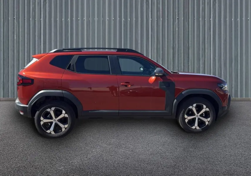 Profil côté gauche d'un Dacia Duster orange 2025 avec barres de toit et jantes alliage 18 pouces.
