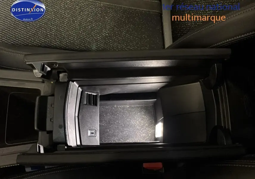 Vue plongeante sur l'accoudoir central ouvert noir de la Peugeot 408 Hybrid 145 GT e-dcs6, intérieur cuir sombre.