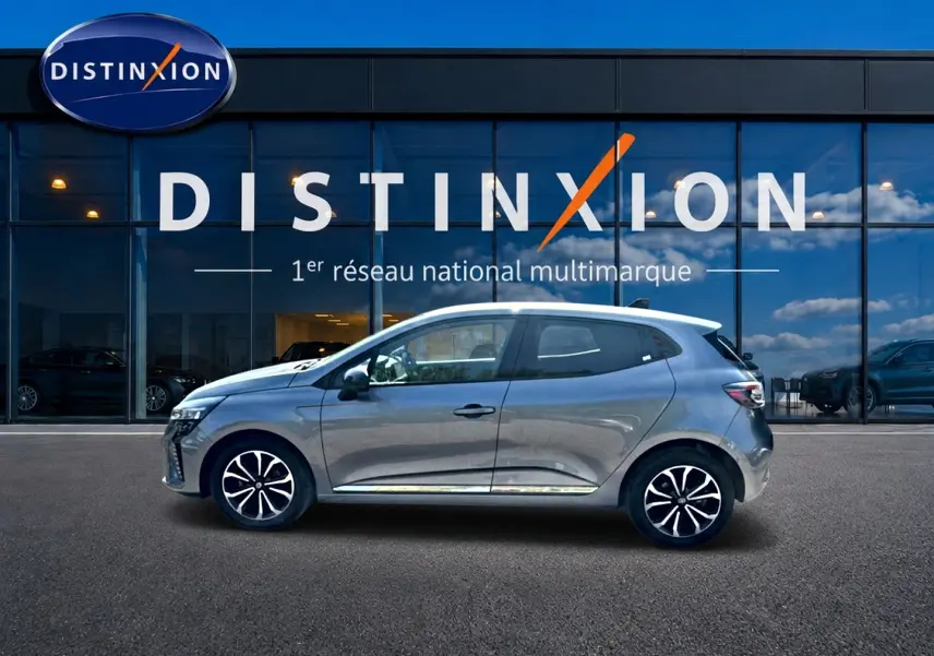 Profil côté gauche de la Renault Clio V gris schiste 2025, avec jantes alu et vitres surteintées devant un showroom Distinxion.
