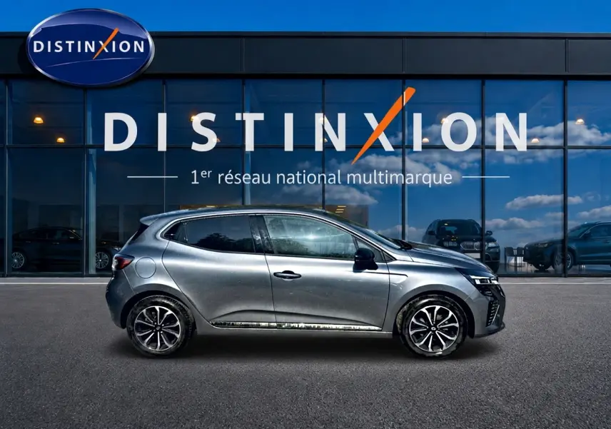 Profil droit de la Renault Clio V gris schiste 2025, avec jantes alu et vitres arrière surteintées, devant un showroom Distinxion.