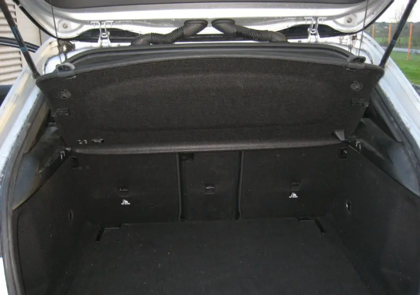Coffre ouvert vu de l'arrière d'une Mercedes Classe A180D gris, montrant l'espace de chargement et la trappe de coffre.