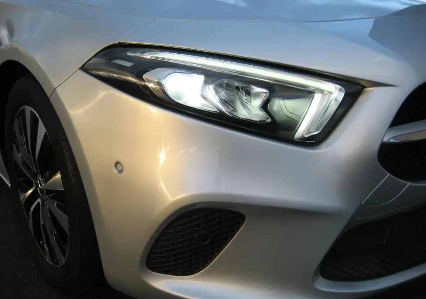 Gros plan sur l'avant droit gris d'une Mercedes Classe A 180d 2021, mettant en valeur le phare LED et la calandre.
