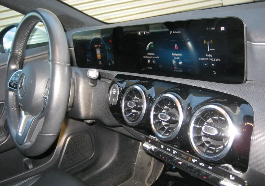 Vue intérieure côté conducteur de la Mercedes Classe A 180d 2021, tableau de bord noir avec écran tactile panoramique et aérateurs ronds chromés.