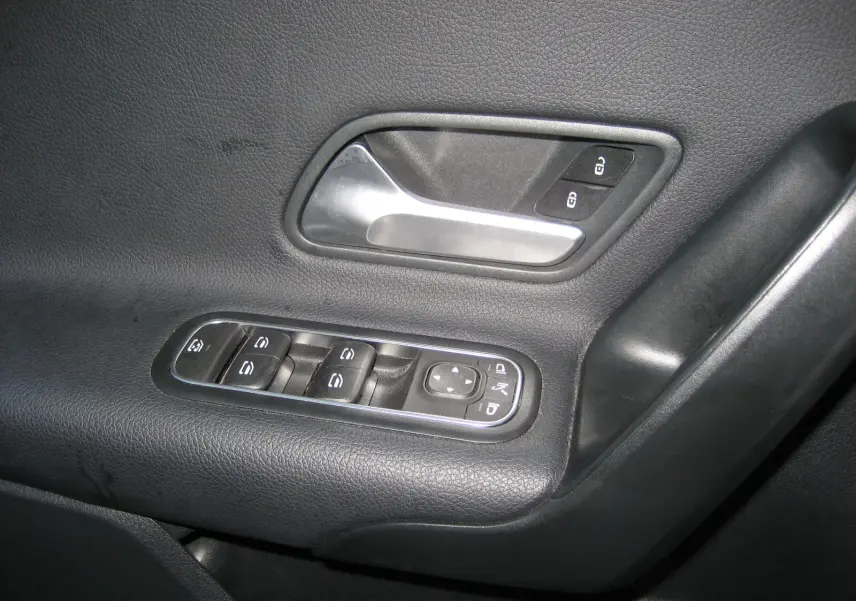 Gros plan sur la poignée intérieure et les commandes des vitres côté gauche d'une Mercedes Classe A gris foncé.