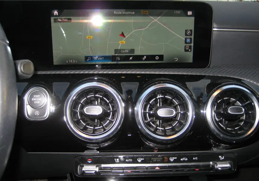 Vue rapprochée de la planche de bord noire d’une Mercedes Classe A 180d 2021 avec écran GPS et aérateurs ronds chromés.