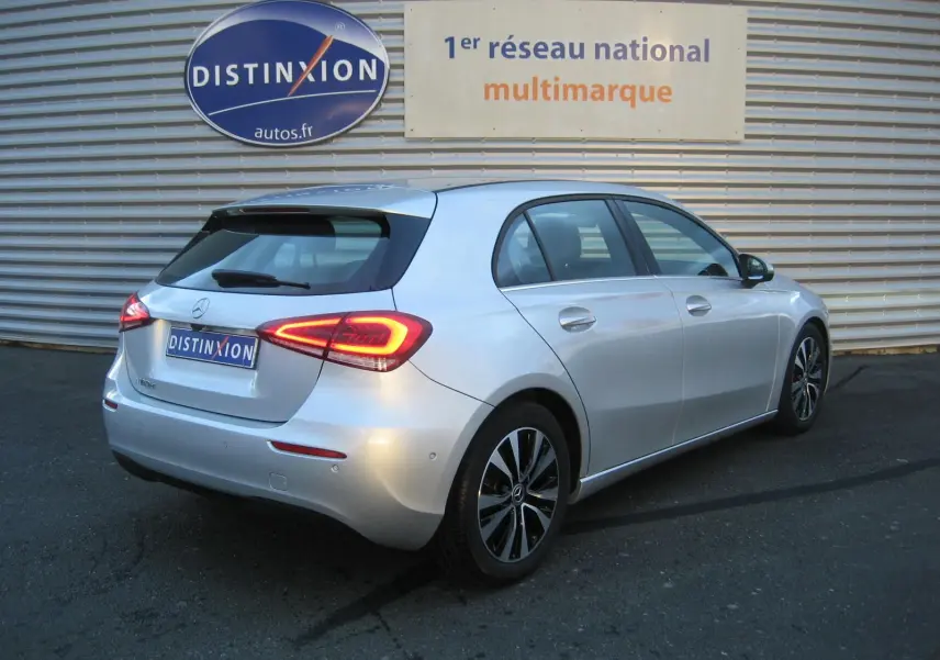 Vue 3/4 arrière droite d'une Mercedes Classe A180D gris métallisé avec feux LED allumés, garée devant un mur métallique.