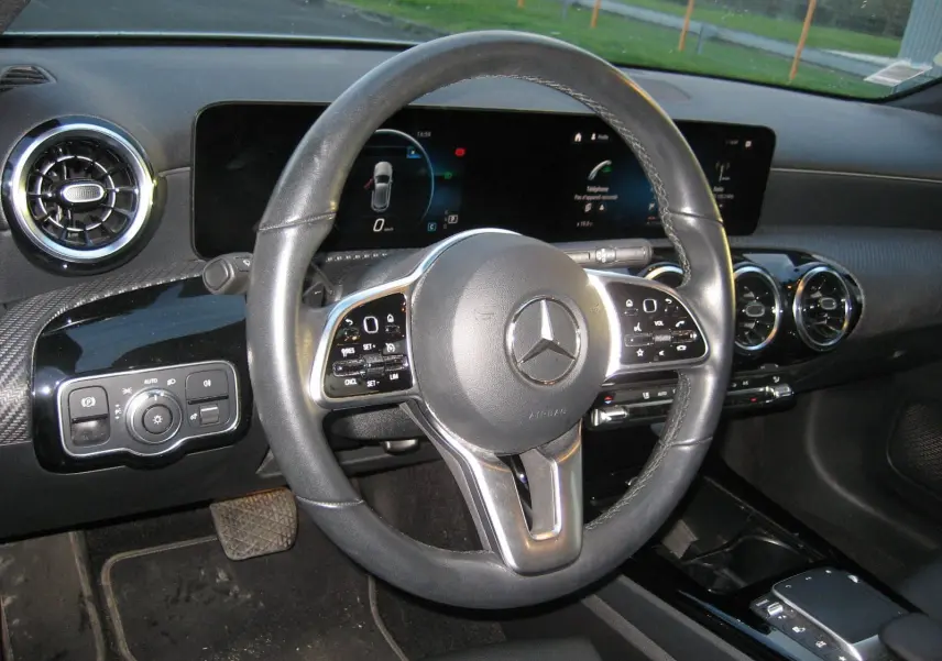 Vue intérieure centrée sur le volant cuir noir d'une Mercedes Classe A 180d 2021 avec tableau de bord numérique.