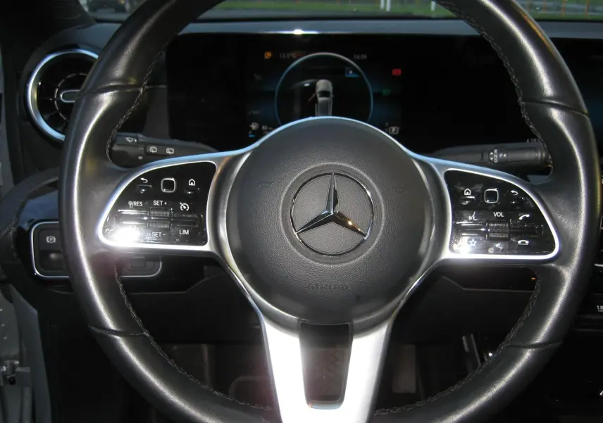 Vue rapprochée du volant cuir noir d’une Mercedes Classe A gris 2021 avec commandes intégrées et écran digital en arrière-plan.