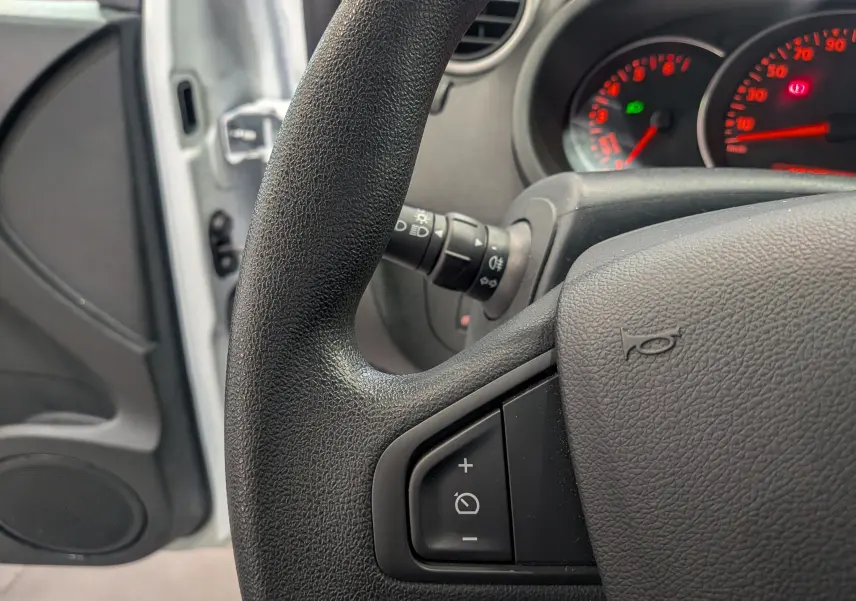 Gros plan sur le volant noir et le tableau de bord rougeoyant du Renault Kangoo Express blanc, côté conducteur ouvert.