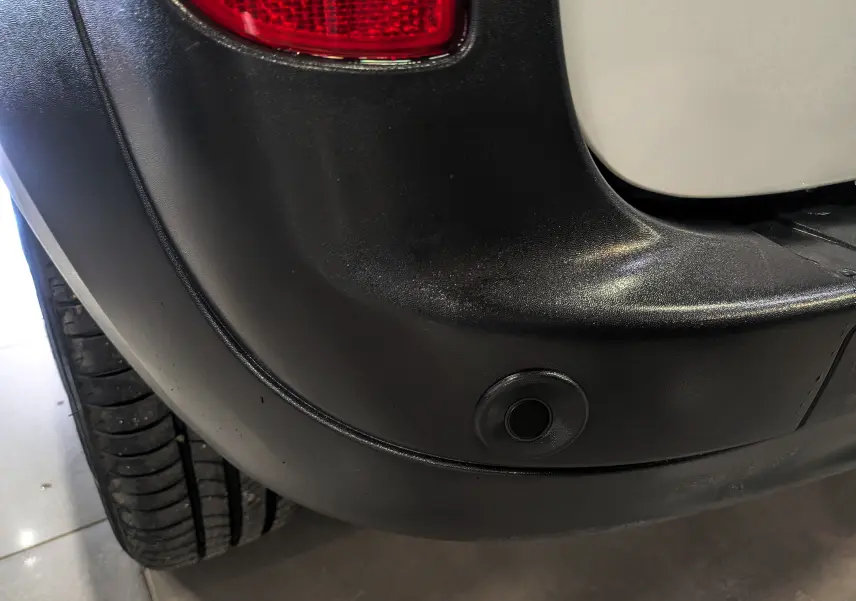 Gros plan sur le pare-chocs arrière droit blanc minéral du Renault Kangoo Express avec capteur de recul visible.