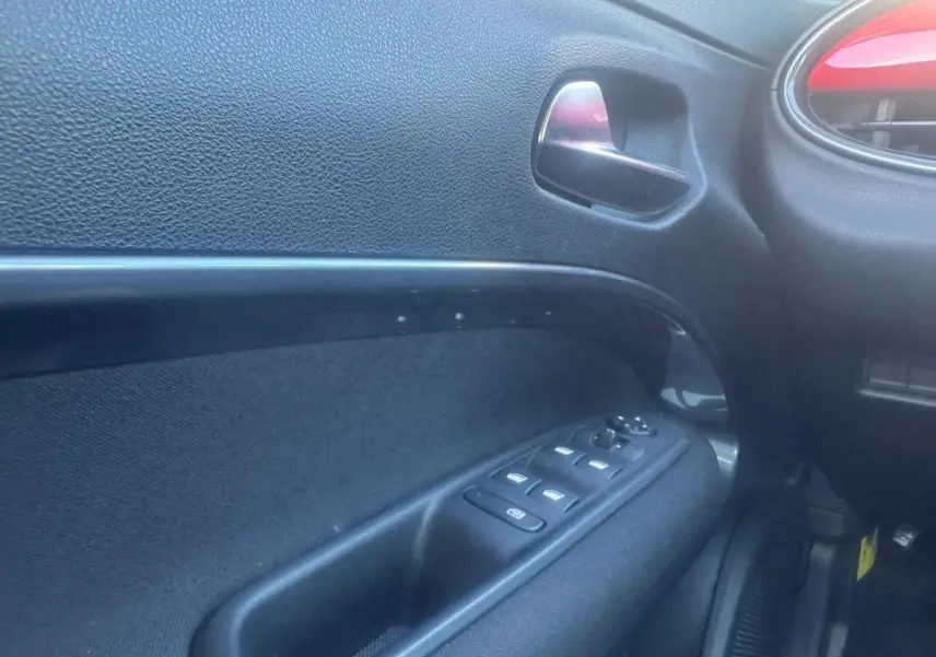 Intérieur de la porte côté gauche de la FIAT 600 rouge 2025, avec commandes électriques des vitres et poignée argentée.