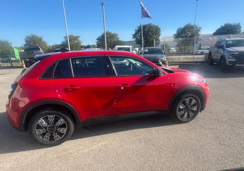 Vue de profil côté gauche d'une FIAT 600 T-Gen 3 rouge 2025 avec jantes noires au design graphique, stationnée en extérieur.