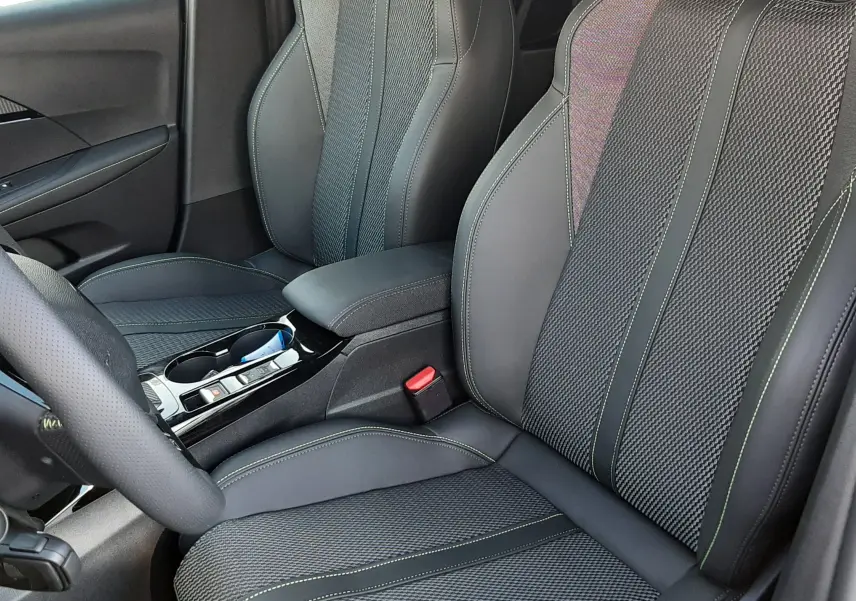 Vue intérieure rapprochée des sièges avant en tissu et cuir noir avec surpiqûres vertes du Peugeot 208 Hybrid 145ch GT.