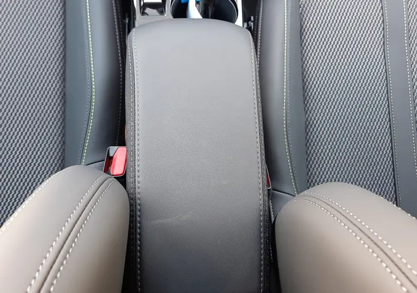 Vue plongeante sur l'accoudoir central noir et les sièges avant en tissu et cuir du Peugeot 208 Hybrid 145ch GT 2026.