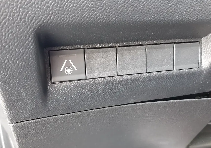 Gros plan sur le bouton d'aide au maintien de voie dans l'habitacle noir d'une Peugeot 208 Hybrid 145ch GT 2026.