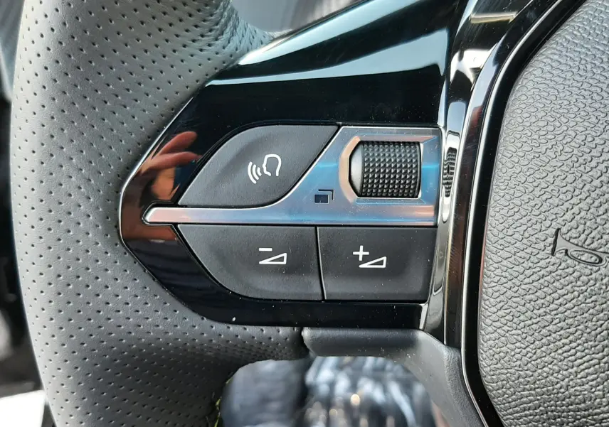 Gros plan sur les commandes noires et chrome du volant perforé du Peugeot 208 Hybrid 145ch GT, côté gauche.
