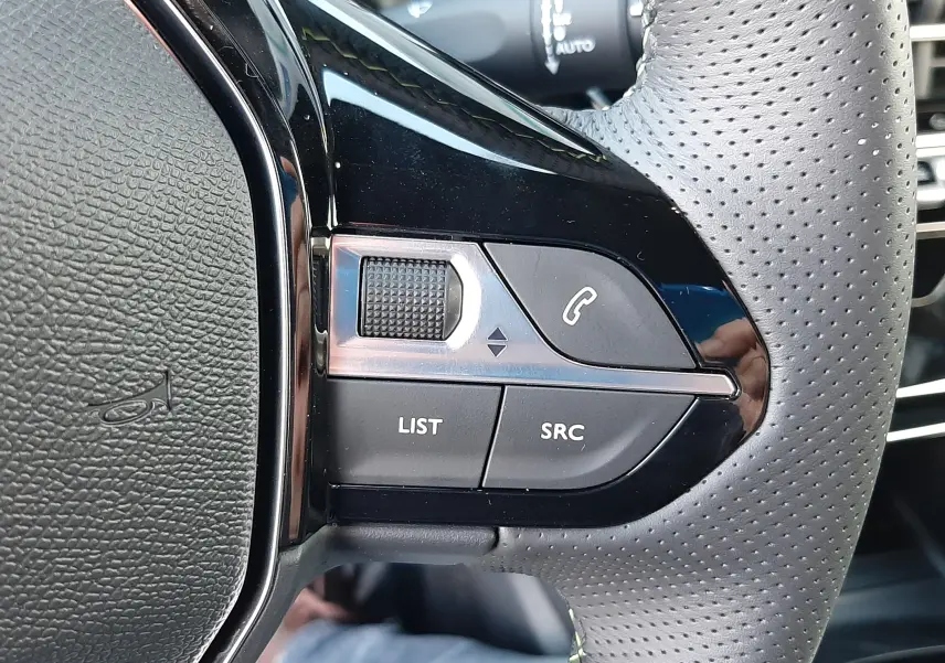 Gros plan sur les commandes gauche du volant perforé noir de la Peugeot 208 Hybrid 145ch GT 2026.