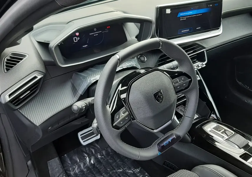 Gros plan sur l'avant gauche noir perla d'une Peugeot 208 Hybrid 145ch GT avec feux LED verticaux allumés sous la pluie.