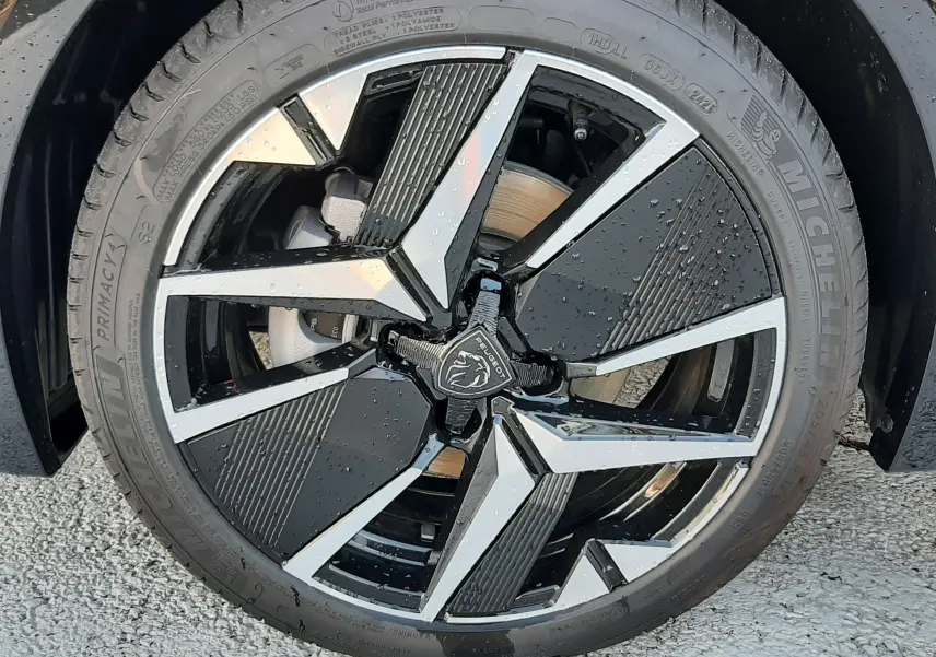 Gros plan sur la jante noire et argentée de la Peugeot 208 Hybrid 145ch GT Perla noire avec logo lion central.