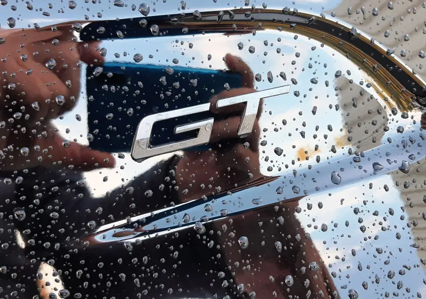Gros plan sur l’inscription GT chromée sur la carrosserie noire perla d’une Peugeot 208 sous gouttes de pluie.