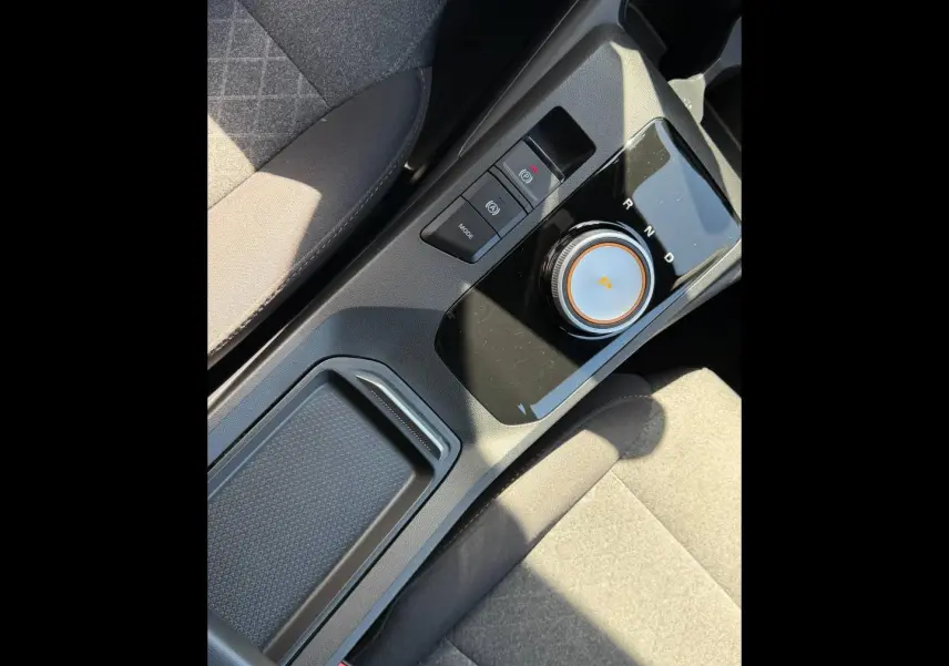 Vue rapprochée de la console centrale noire avec molette de boîte auto et tissu gris du siège MG3 blanc 2025.