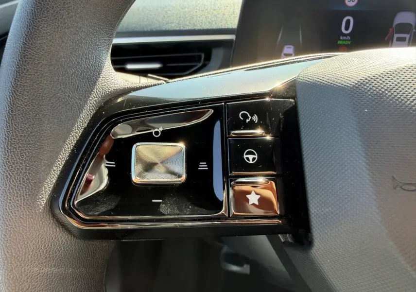 Gros plan sur les commandes noires du volant côté gauche du MG3 blanc hybride 2025 avec écran numérique en arrière-plan.
