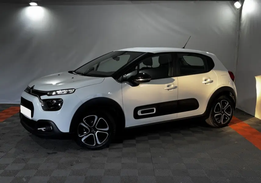 Citroën C3 blanche vue de profil droit en intérieur, avec protections latérales noires et jantes stylisées.