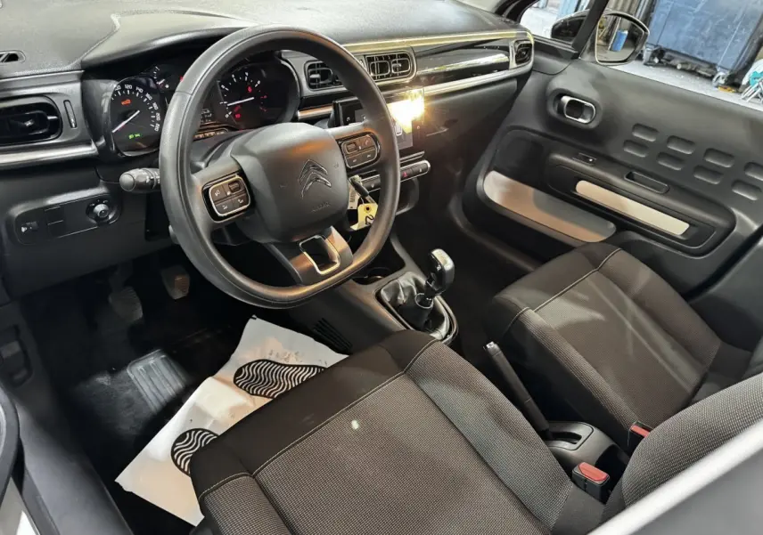 Intérieur de la Citroën C3 2024 vu côté conducteur, volant multifonctions, tableau de bord noir et sièges tissu gris.