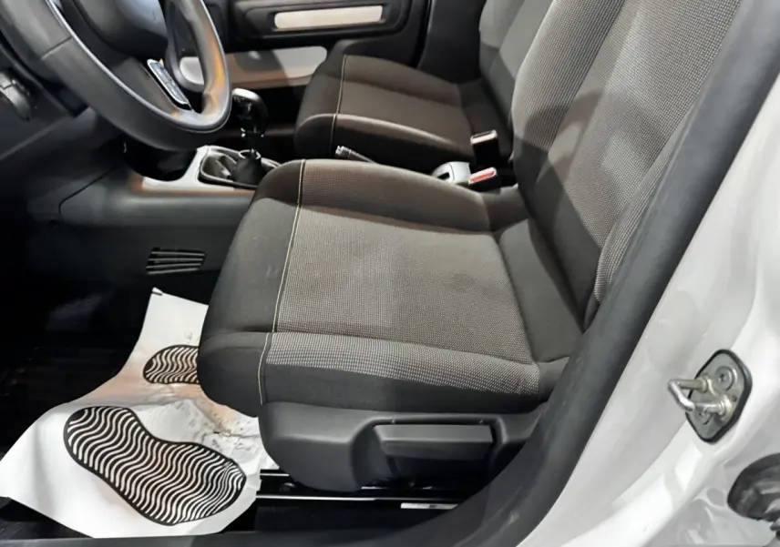 Vue intérieure côté conducteur de la Citroën C3 blanche 2024, montrant les sièges avant en tissu gris et la boîte manuelle.