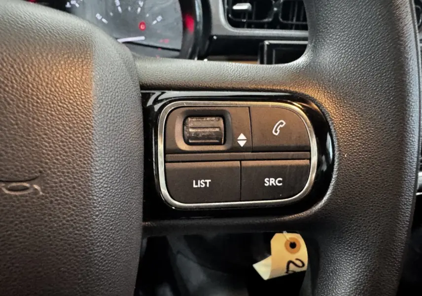 Gros plan sur les commandes multifonctions du volant noir d’une Citroën C3 PureTech 2024, intérieur sombre.