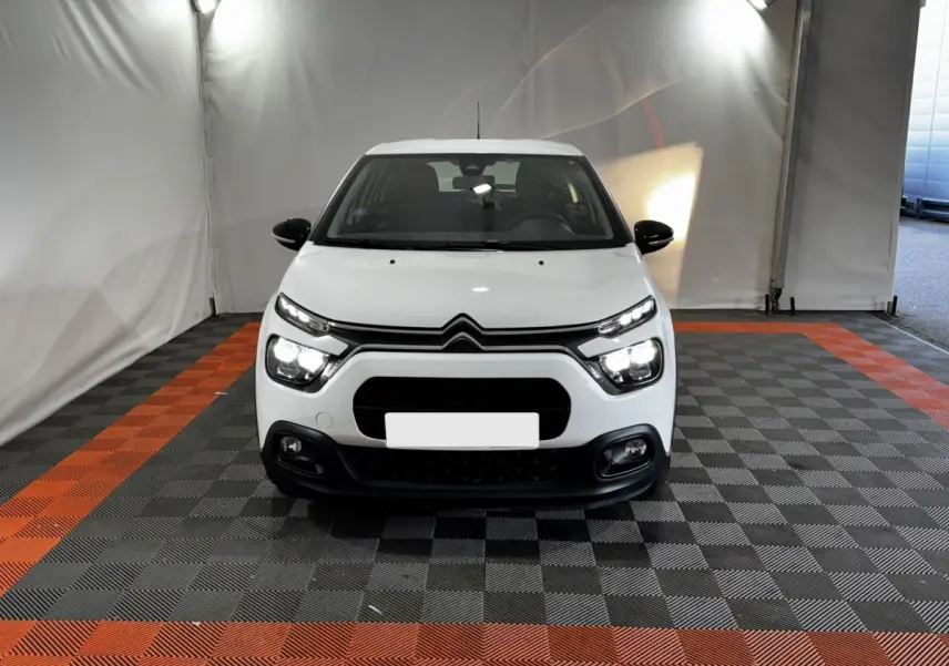 Vue frontale d'une Citroën C3 blanche 2024 avec phares LED allumés dans un garage éclairé.
