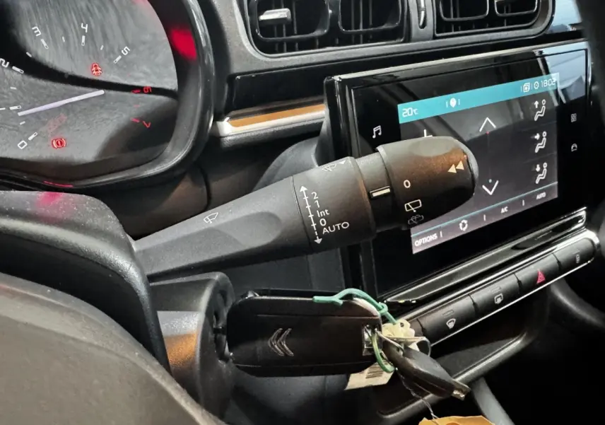 Gros plan intérieur sur le tableau de bord et la clé de contact d’une Citroën C3 blanche, avec écran tactile et commandes au volant.