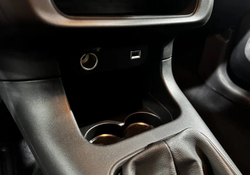 Gros plan sur la console centrale noire de la Citroën C3 avec prise 12V, port USB et emplacement porte-gobelets.