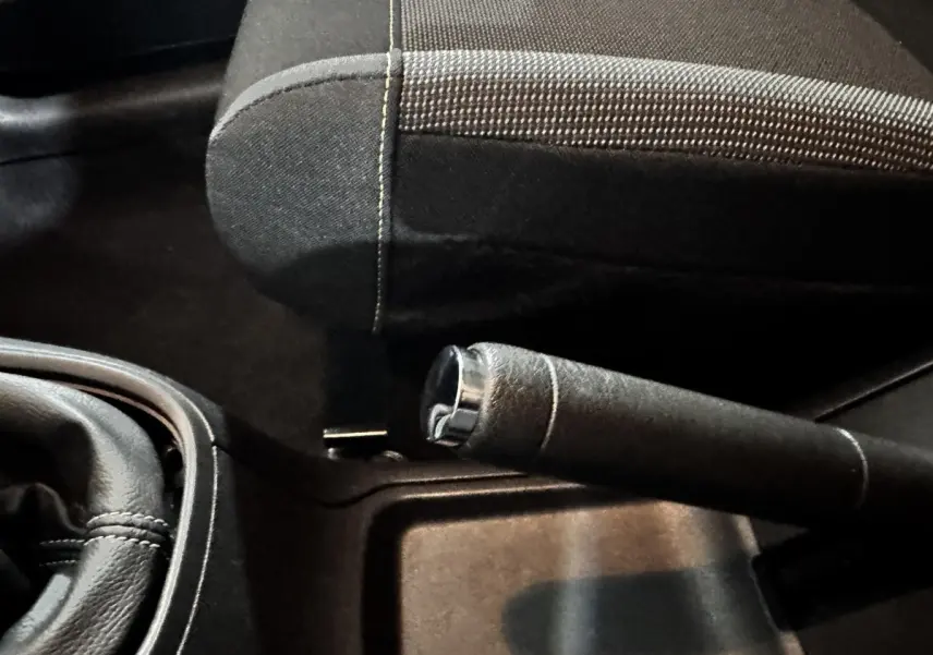 Gros plan sur le frein à main et le siège avant en tissu noir de la Citroën C3 PureTech 83 blanche, intérieur sombre.