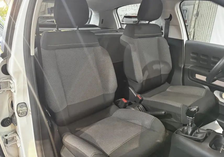 Vue intérieure de face des sièges avant gris foncé de la Citroën C3 blanche, avec levier de vitesse manuel visible.