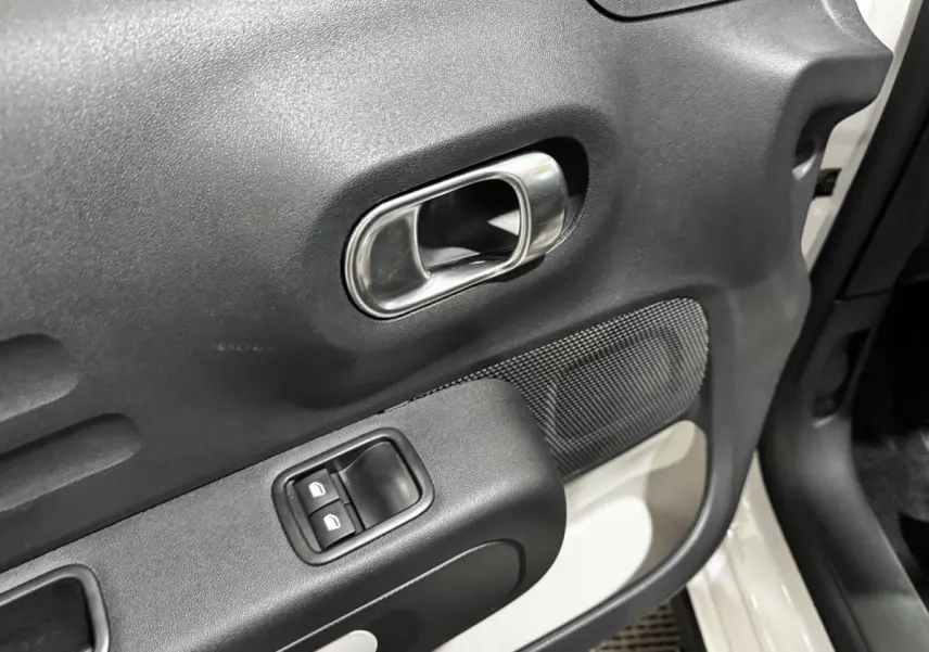 Gros plan sur la porte avant droite blanche d’une Citroën C3 2024, avec poignée intérieure chromée et commandes de vitres.