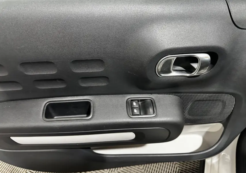Détail de la porte intérieure côté conducteur de la Citroën C3 blanche 2024 avec commandes de vitres et poignée chromée.