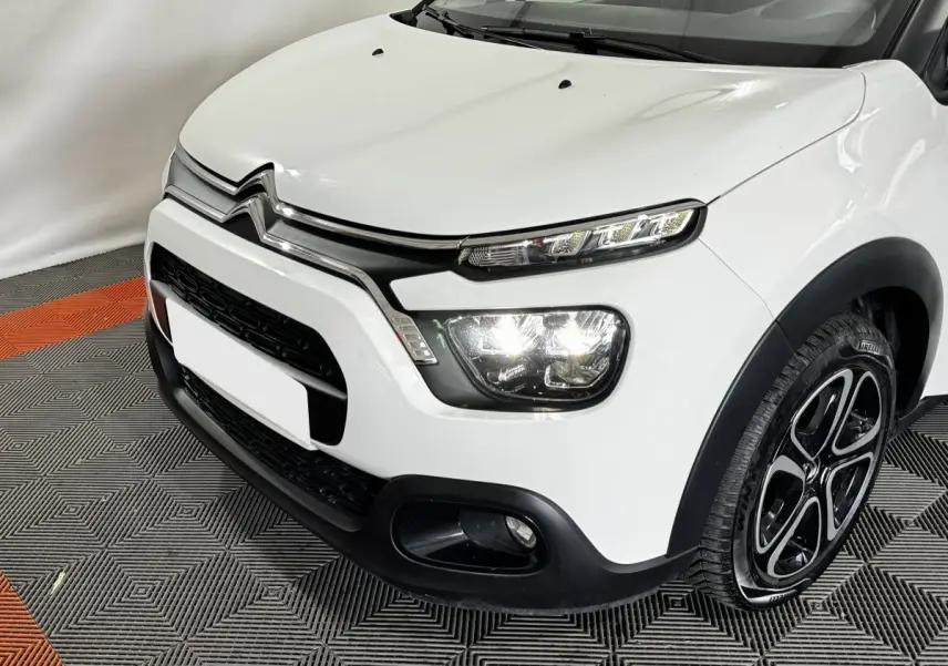 Vue 3/4 avant droit d'une Citroën C3 blanche 2024 avec phares LED allumés et jantes noires à motifs.